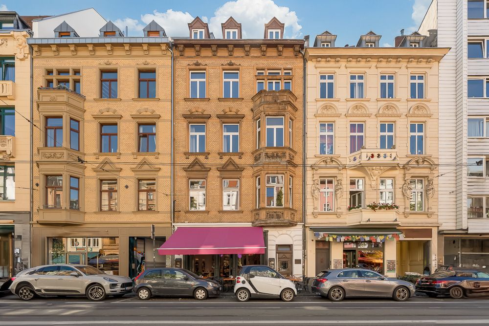 Drei mehrstöckige Wohngebäude mit Erkern und geparkten Autos davor.