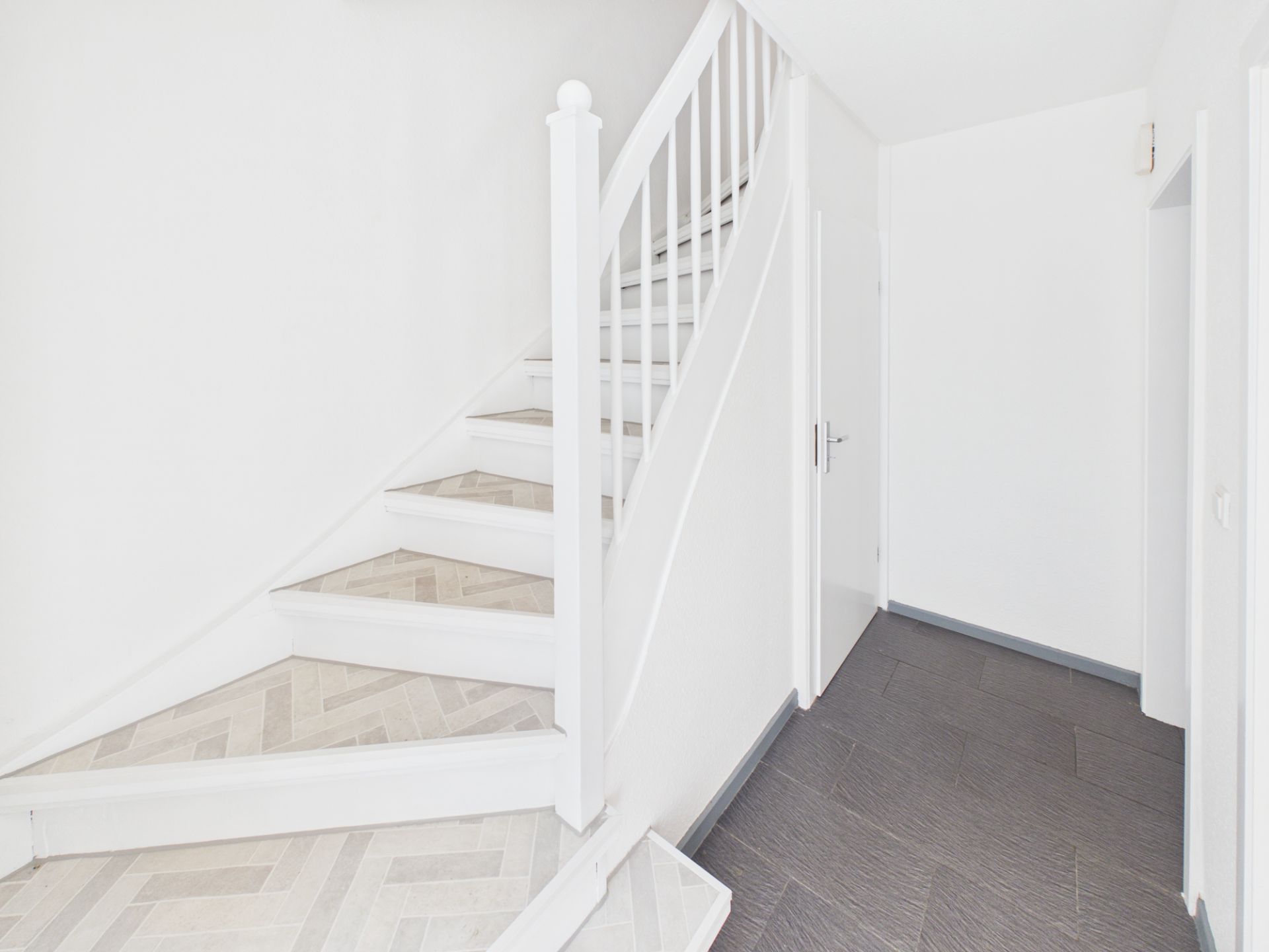 Heller Flur mit weißer Treppe und angrenzenden Türen.