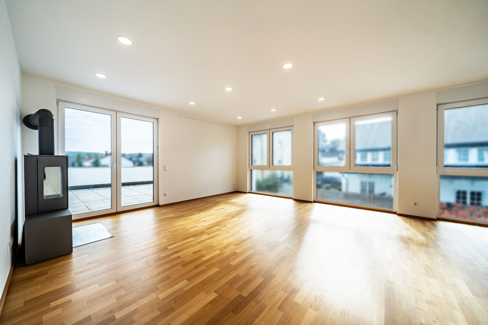 Helles Wohnzimmer mit Holzboden, vielen Fenstern und einem Kaminofen.