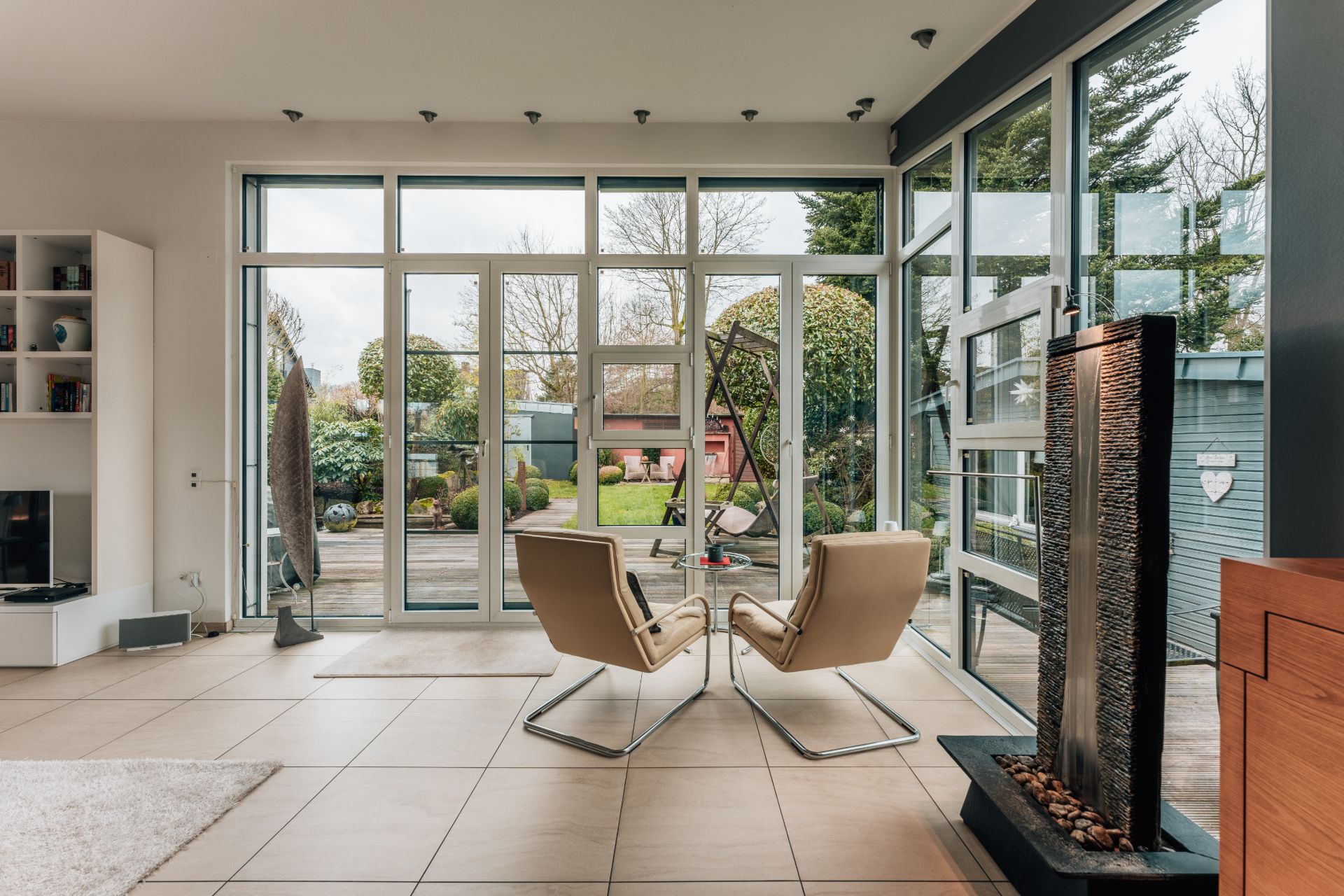Helles Wohnzimmer mit zwei Sesseln, Glastüren und Blick auf einen gepflegten Garten.