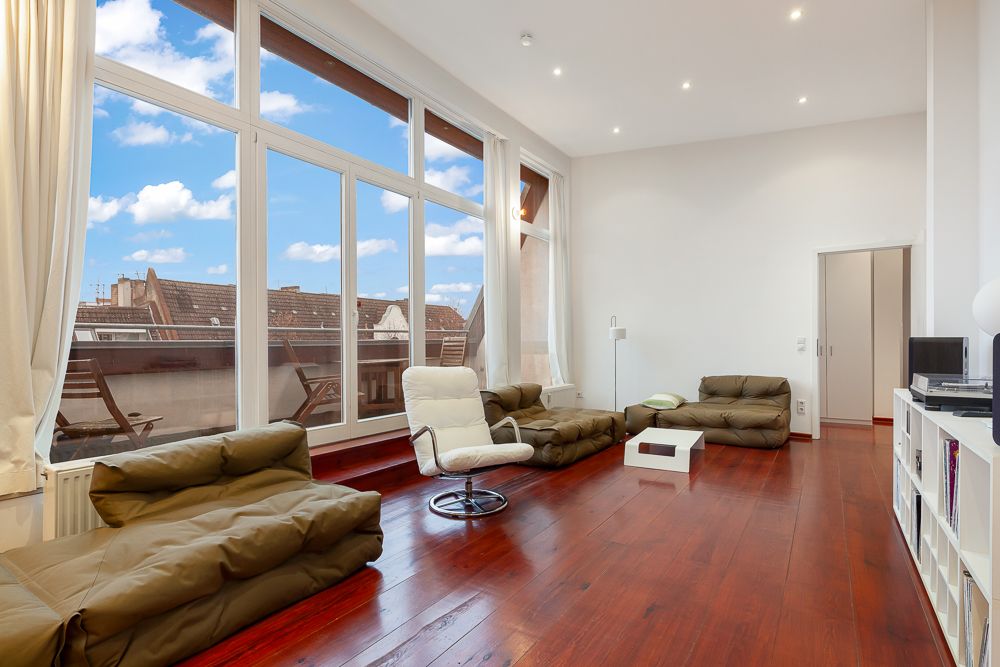 Modernes Wohnzimmer mit großen Fenstern, braunem Holzboden und bequemen Sitzmöbeln.