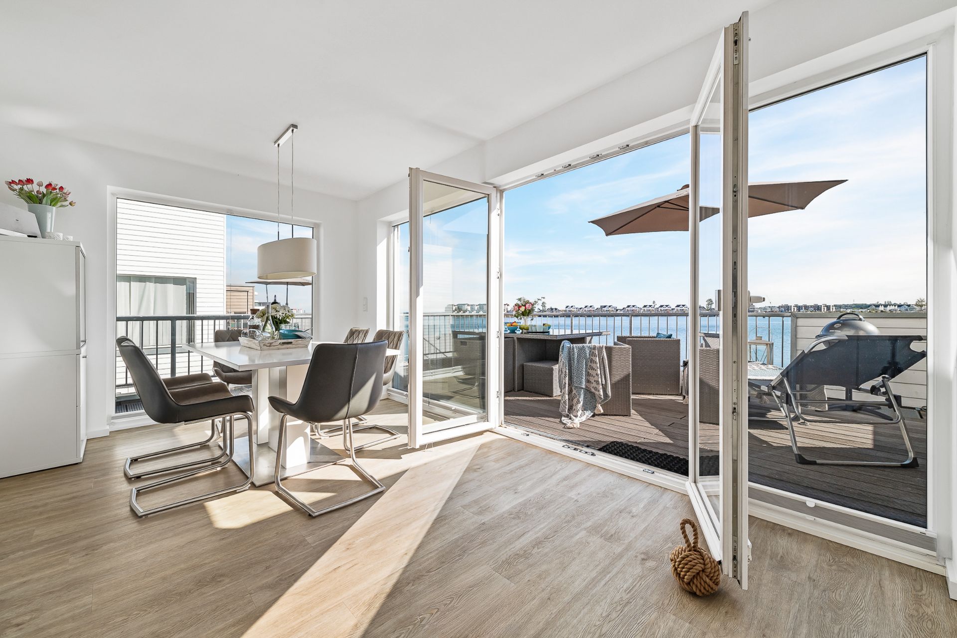 Helles Esszimmer mit Glastüren zu Terrasse mit Sitzgruppe und Seeblick.