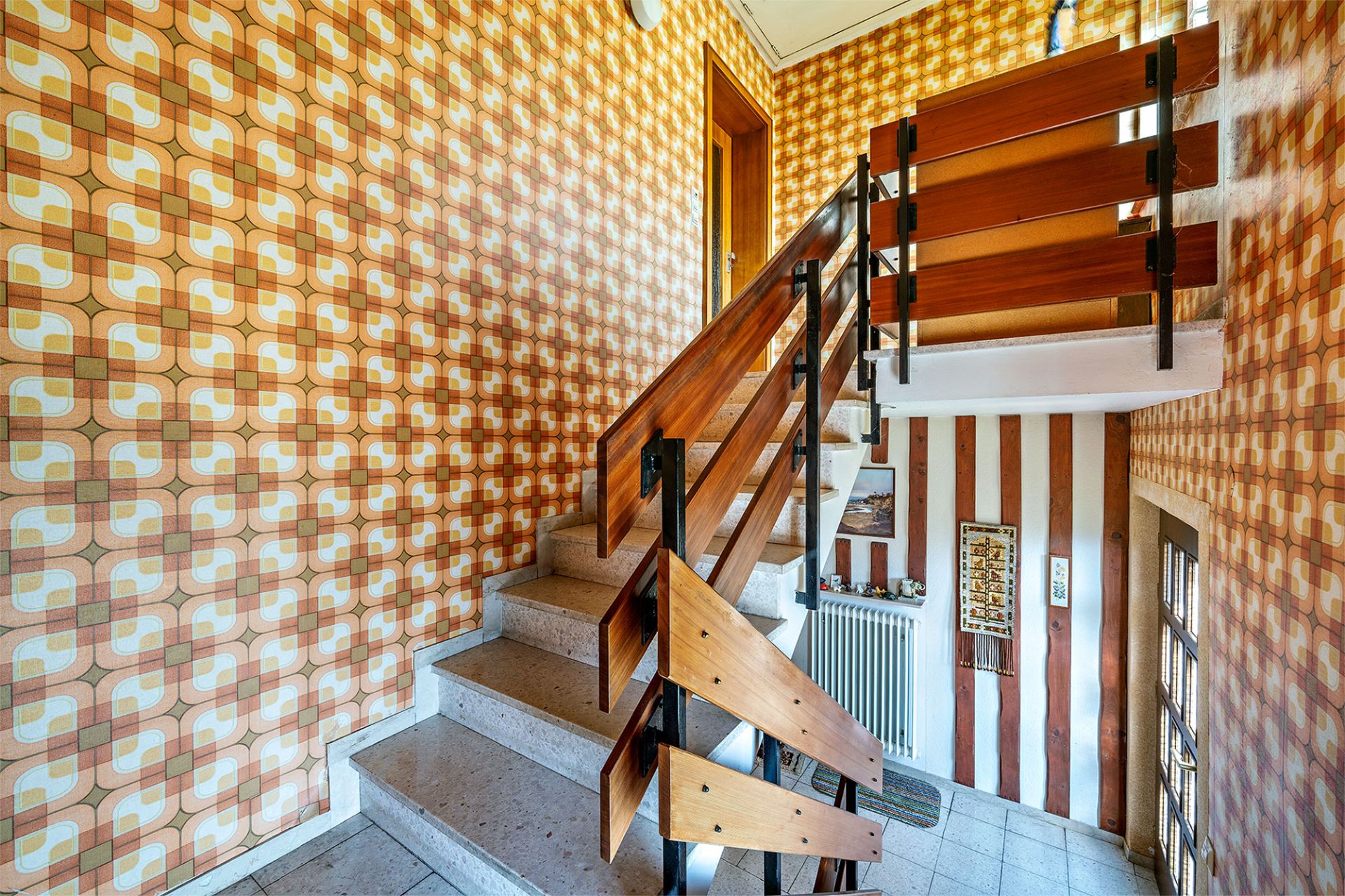 Treppenhaus mit bunten Retro-Tapeten und Holzgeländer in einem Wohnhaus.