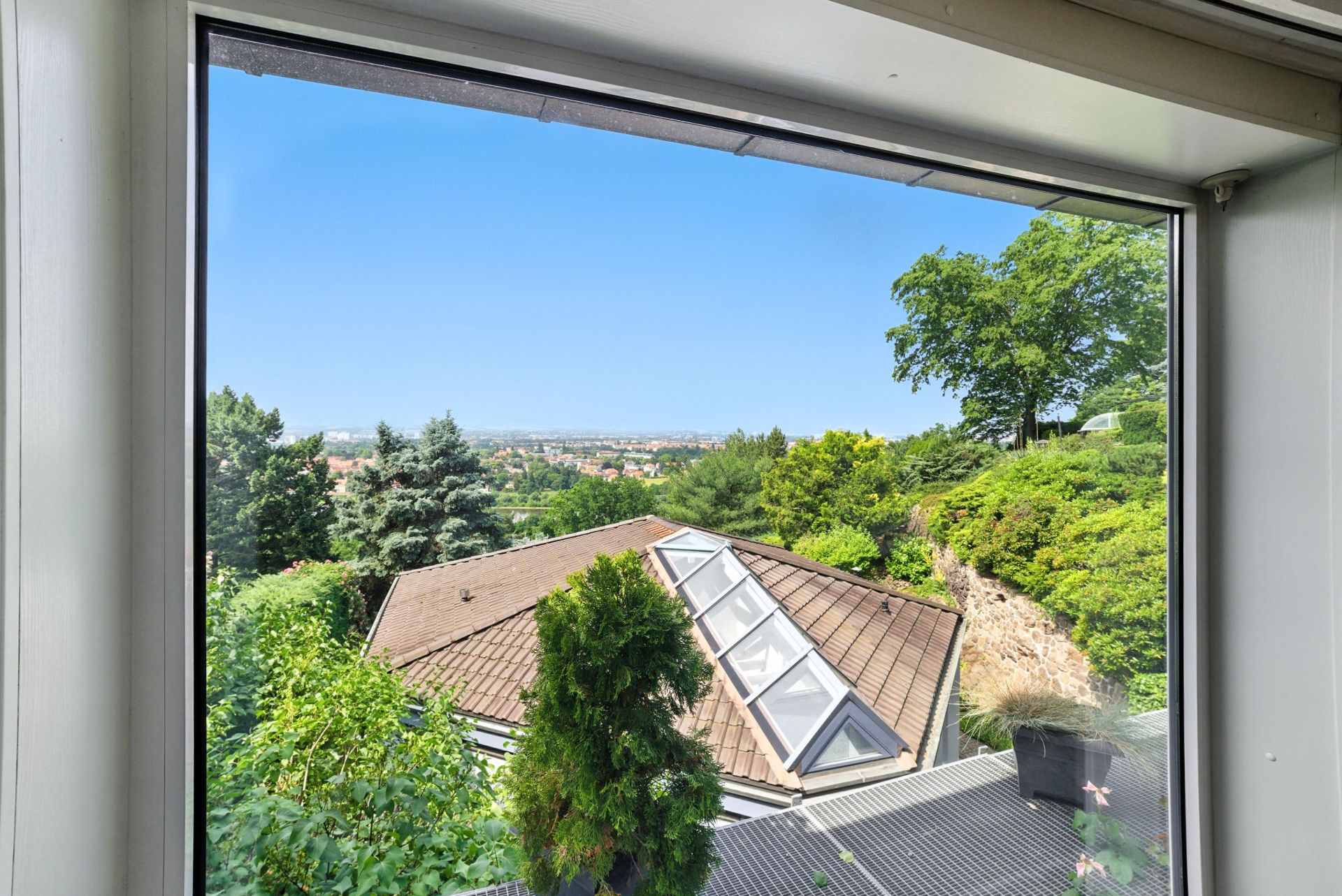 Blick aus einem Fenster auf ein begrüntes Dach und Bäume im Garten.