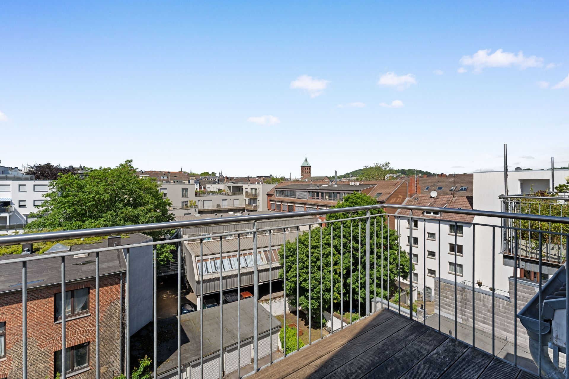 Blick von einem Balkon auf Wohngebäude und Bäume unter blauem Himmel.