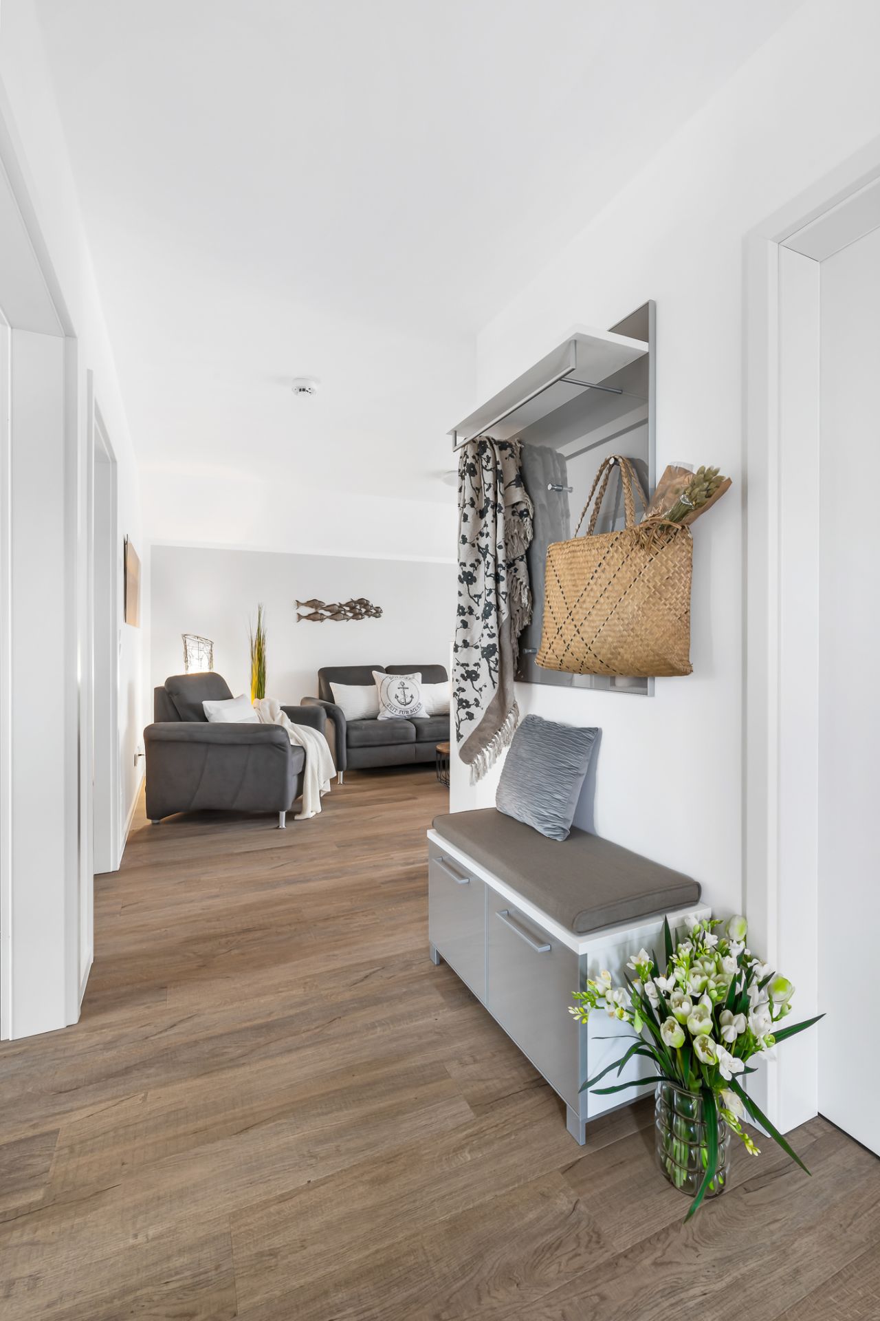 Heller Flur mit Sitzbank, Garderobe, Blumen und Blick ins Wohnzimmer mit Sesseln.