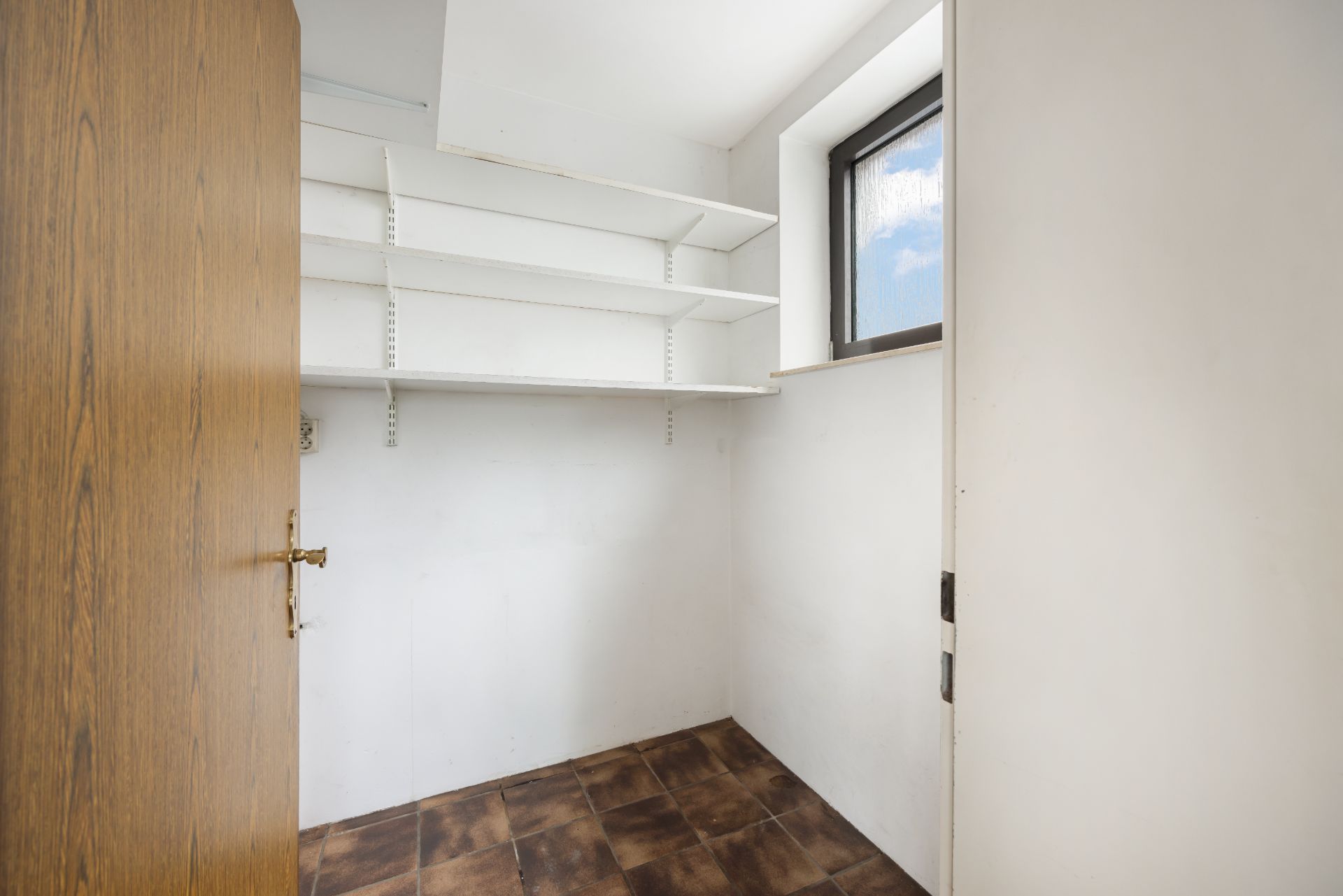 Kleiner Raum mit Wandregalen, braunem Fliesenboden und Fenster.