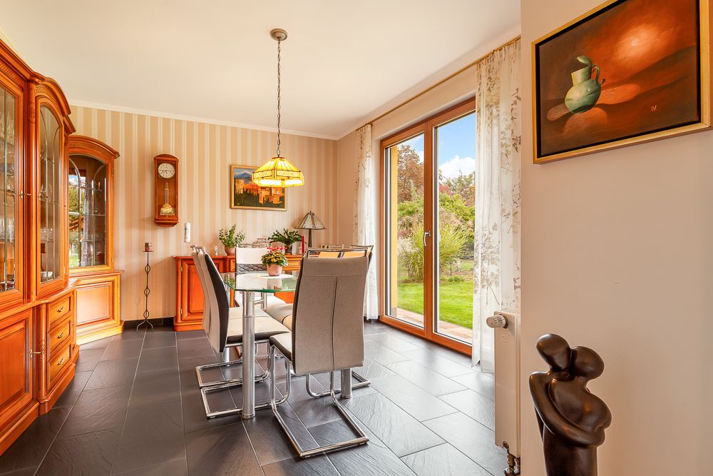 Esszimmer mit Glastisch, sechs Stühlen, Holzmöbeln und großen Fenstern zum Garten.
