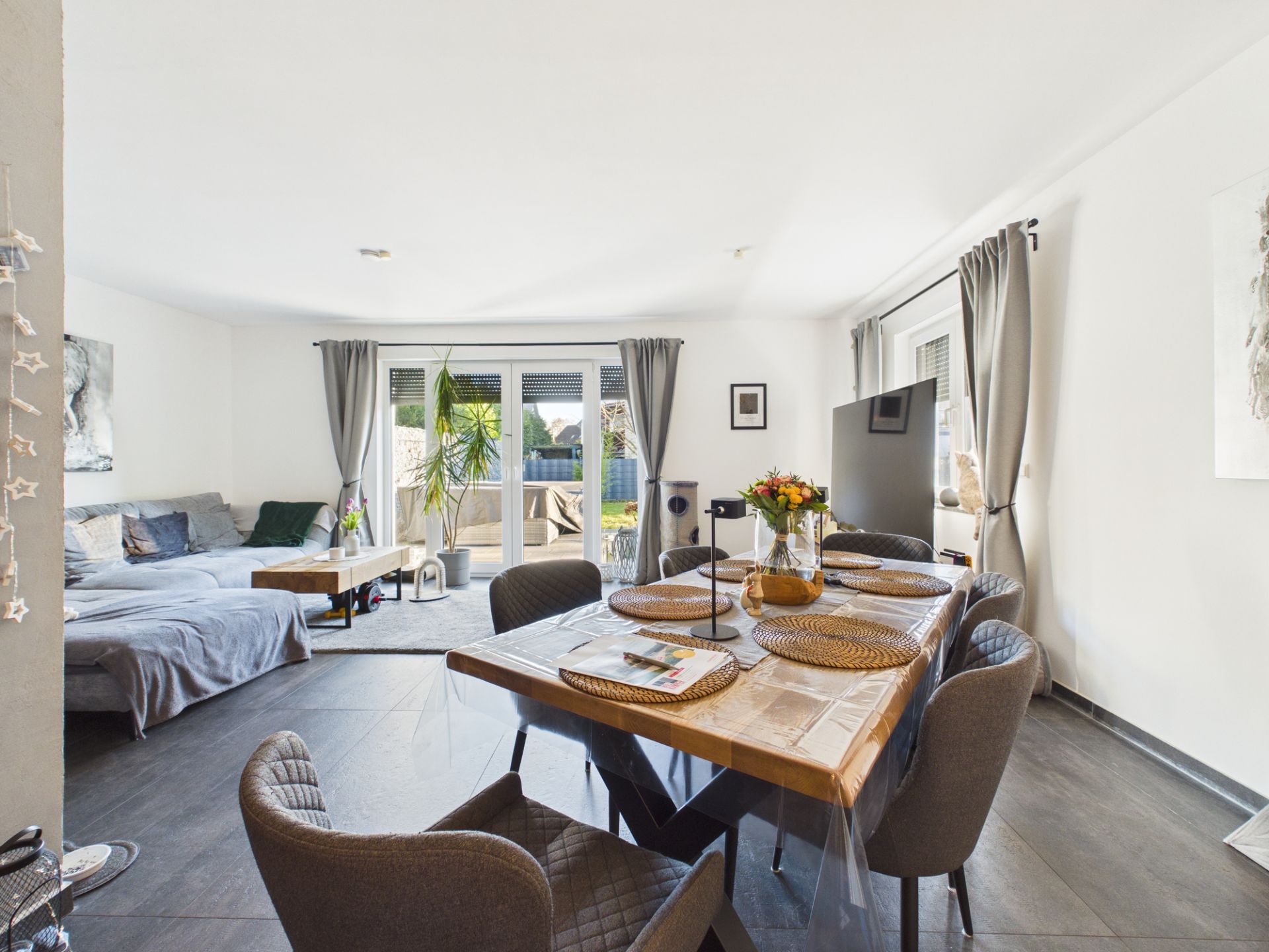 Helles Wohnzimmer mit Essbereich, Sofa, Esstisch und Zugang zum Garten durch Glastür.