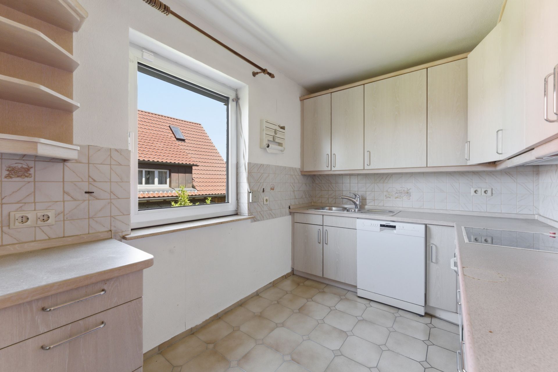 Helle Einbauküche mit Fenster, Spüle, Geschirrspüler und weißen Schränken.