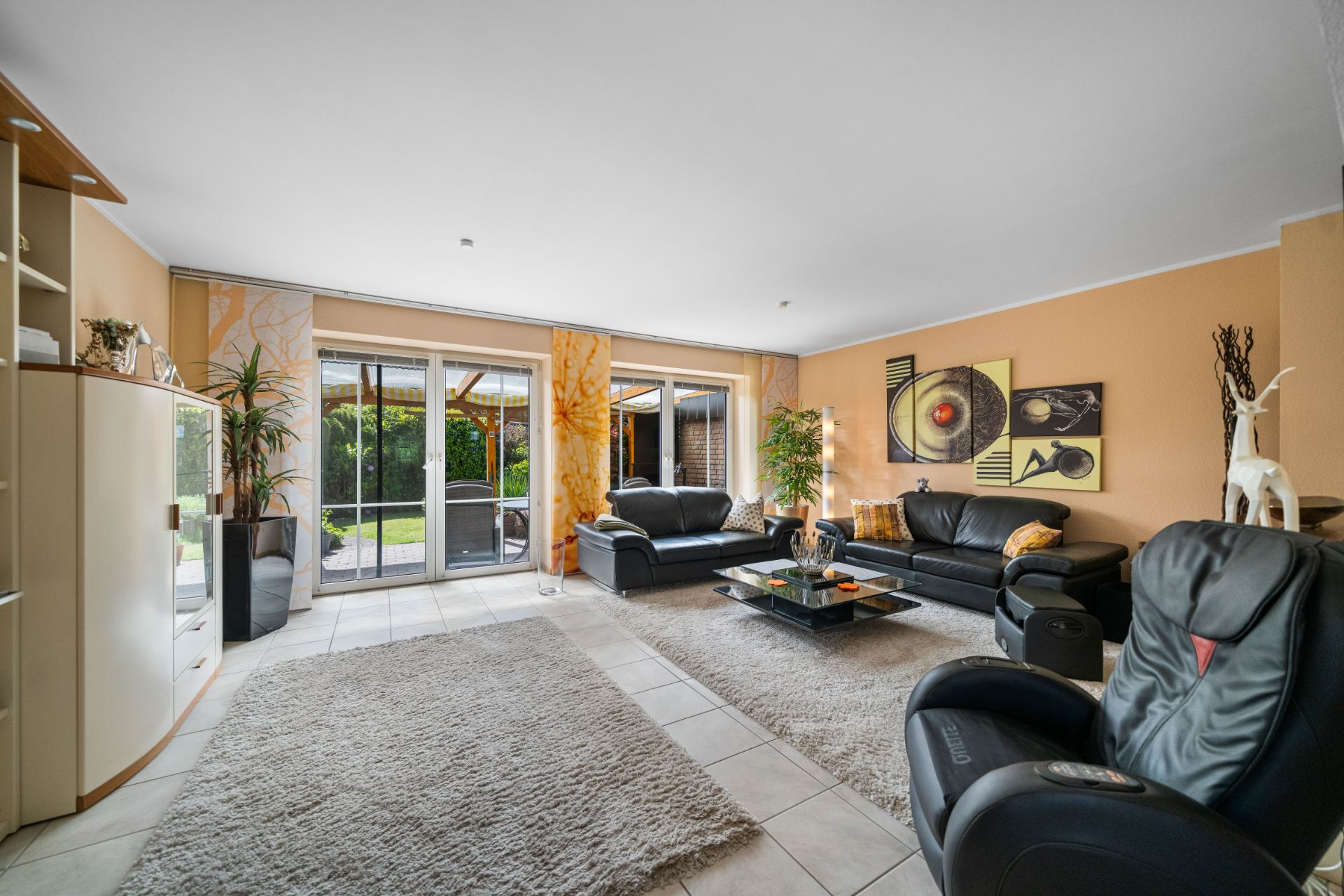 Modernes Wohnzimmer mit Ledersofas, Teppich, großen Fenstern und Wanddeko, Blick in den Garten.