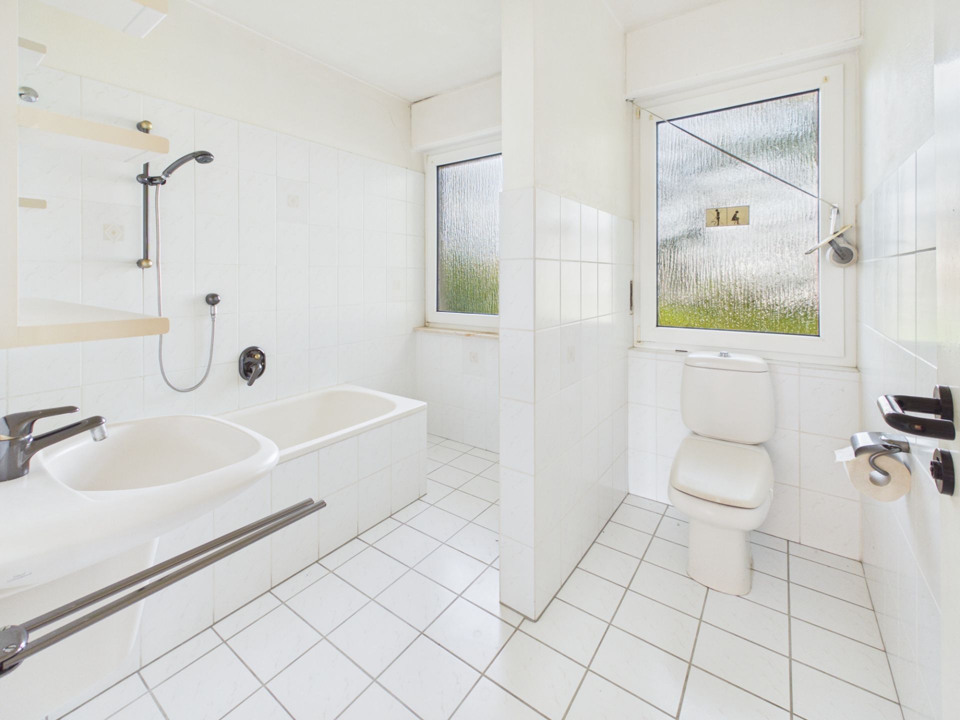 Helles Badezimmer mit Badewanne, Waschbecken, Toilette und zwei Fenstern.