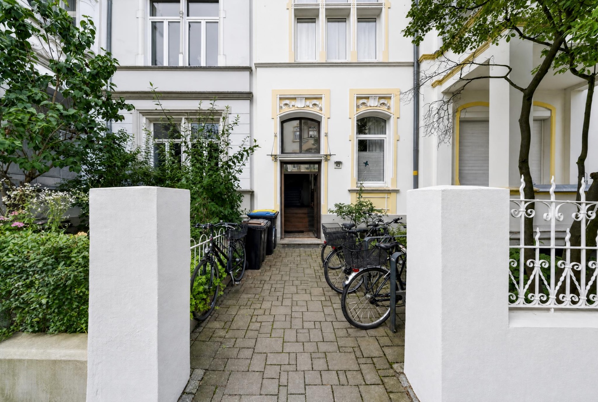 Eingang eines Wohnhauses mit Fahrrädern und einem gepflasterten Weg im Vorgarten.
