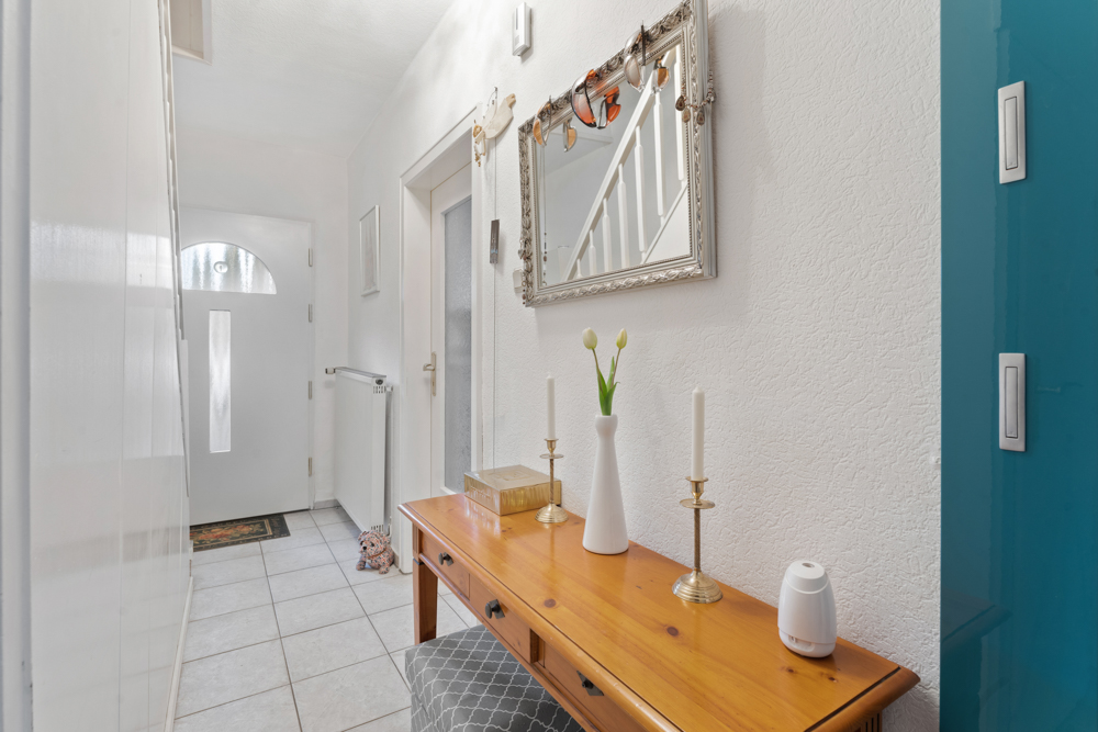 Heller Flur mit Holztisch, Spiegel, Kerzenhaltern und Vase mit Blumen.
