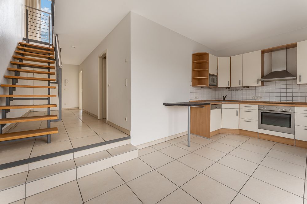 Helle Wohnküche mit Treppe, Einbauküche und Fliesenboden.