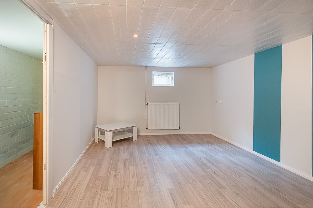 Heller Raum mit Holzfußboden, kleinem Fenster, Heizkörper und kleinem weißen Tisch.