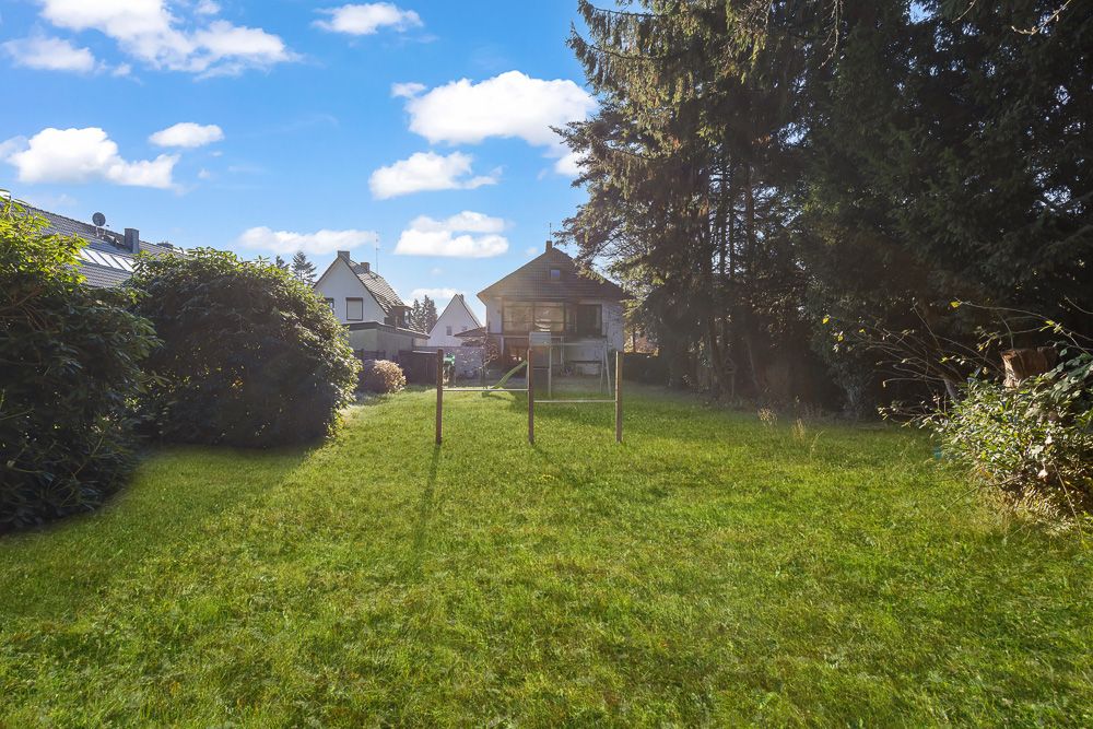 Grüner Garten mit Rasen, Wäscheleinen und einem Wohnhaus im Hintergrund.