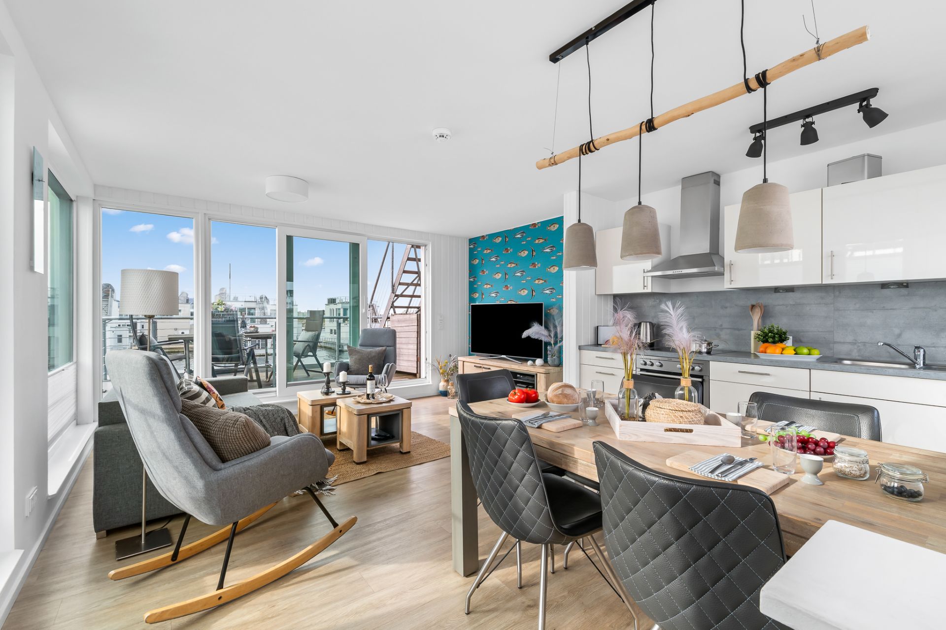 Helles Wohnzimmer mit offener Küche, Esstisch und Zugang zu einem Balkon mit Stadtblick.