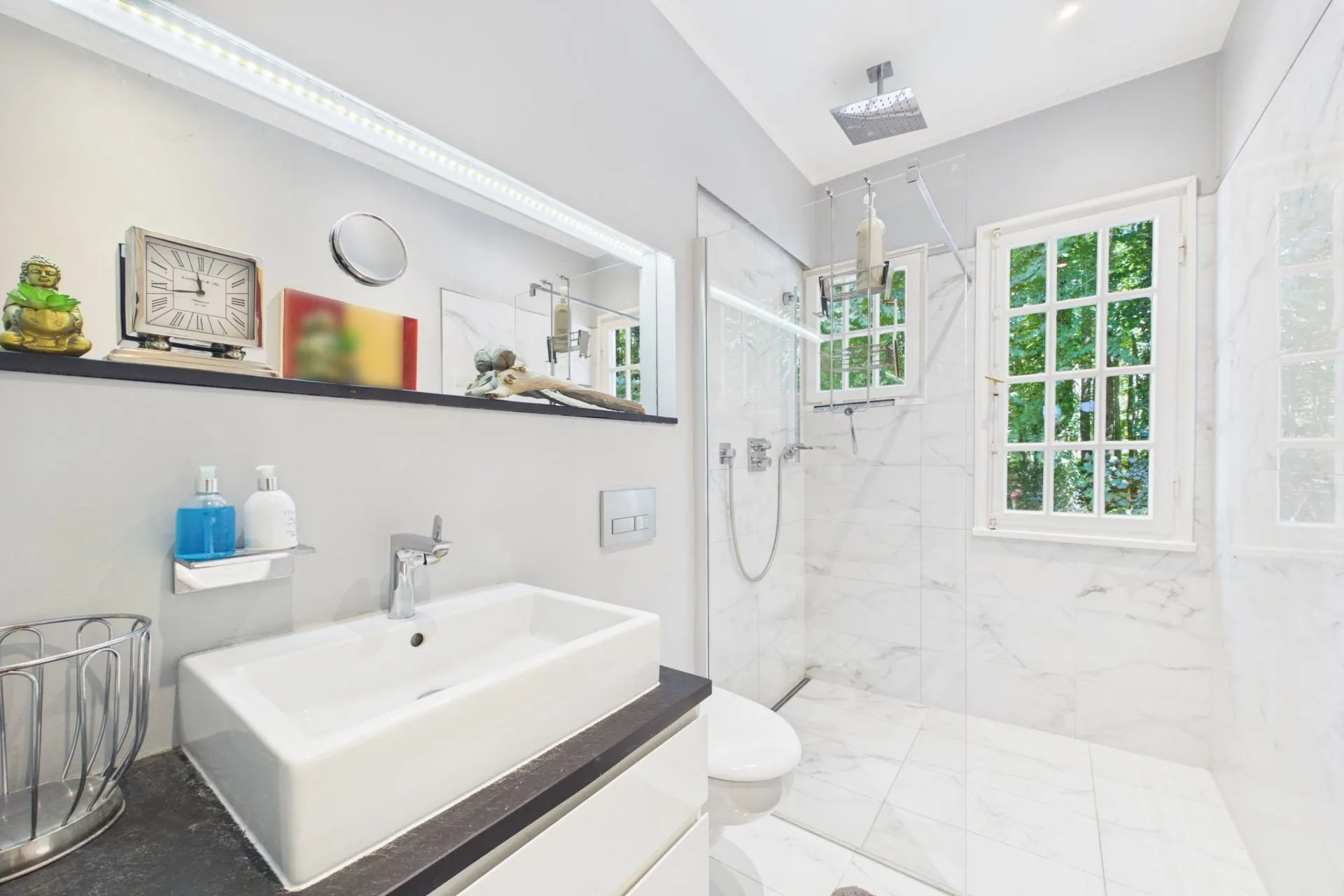 Modernes Badezimmer mit Dusche, Waschbecken, großem Spiegel und Fenster mit Blick ins Grüne.