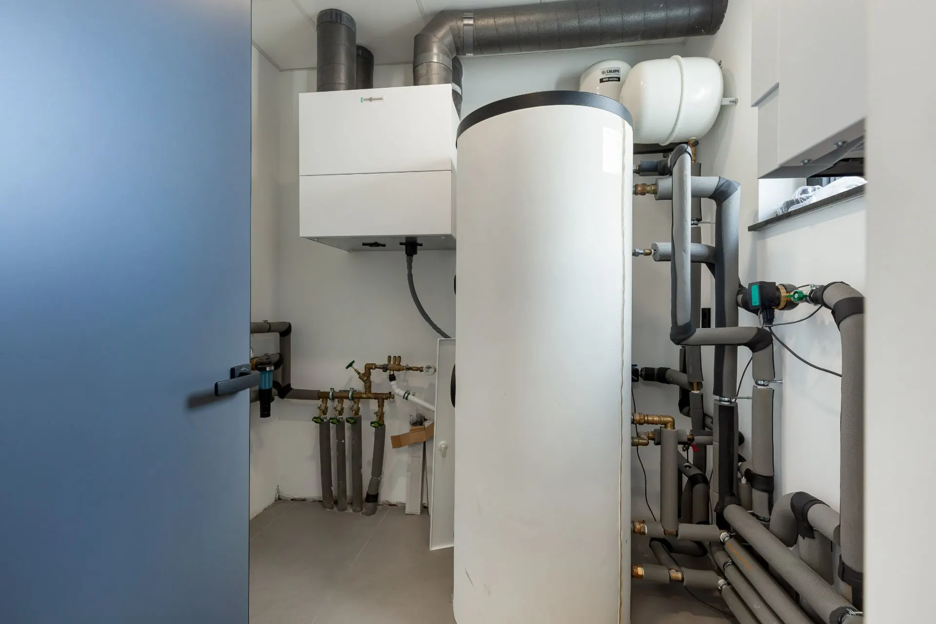 Technikraum mit großem Warmwasserspeicher, Rohren und Heizungsanlage.