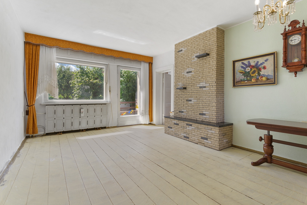 Helles Wohnzimmer mit großem Fenster, gelben Vorhängen, Kamin, Uhr und Bild an der Wand.