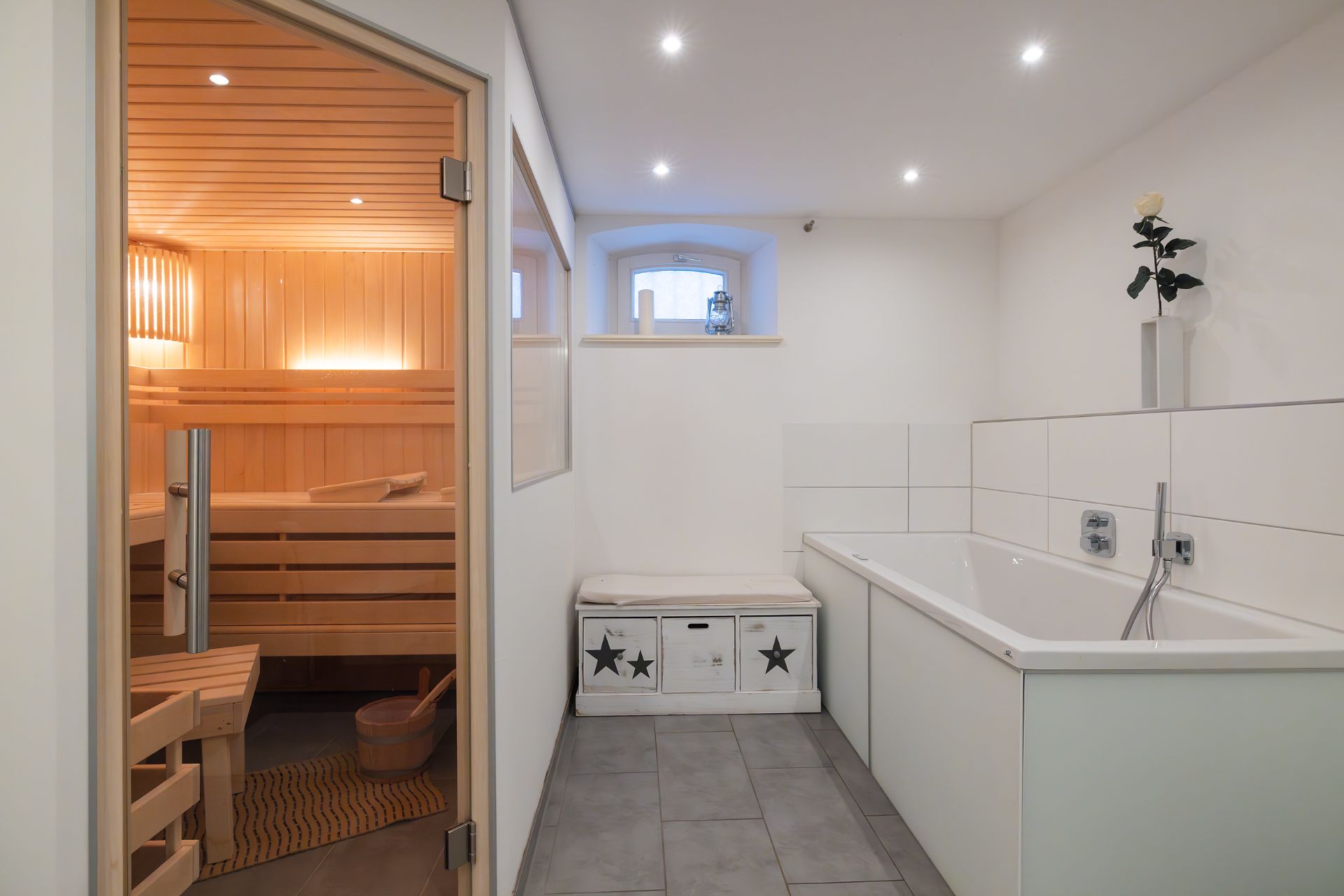 Modernes Badezimmer mit Sauna, Badewanne, Sitzbank und dekorativer Vase auf heller Fensterbank.