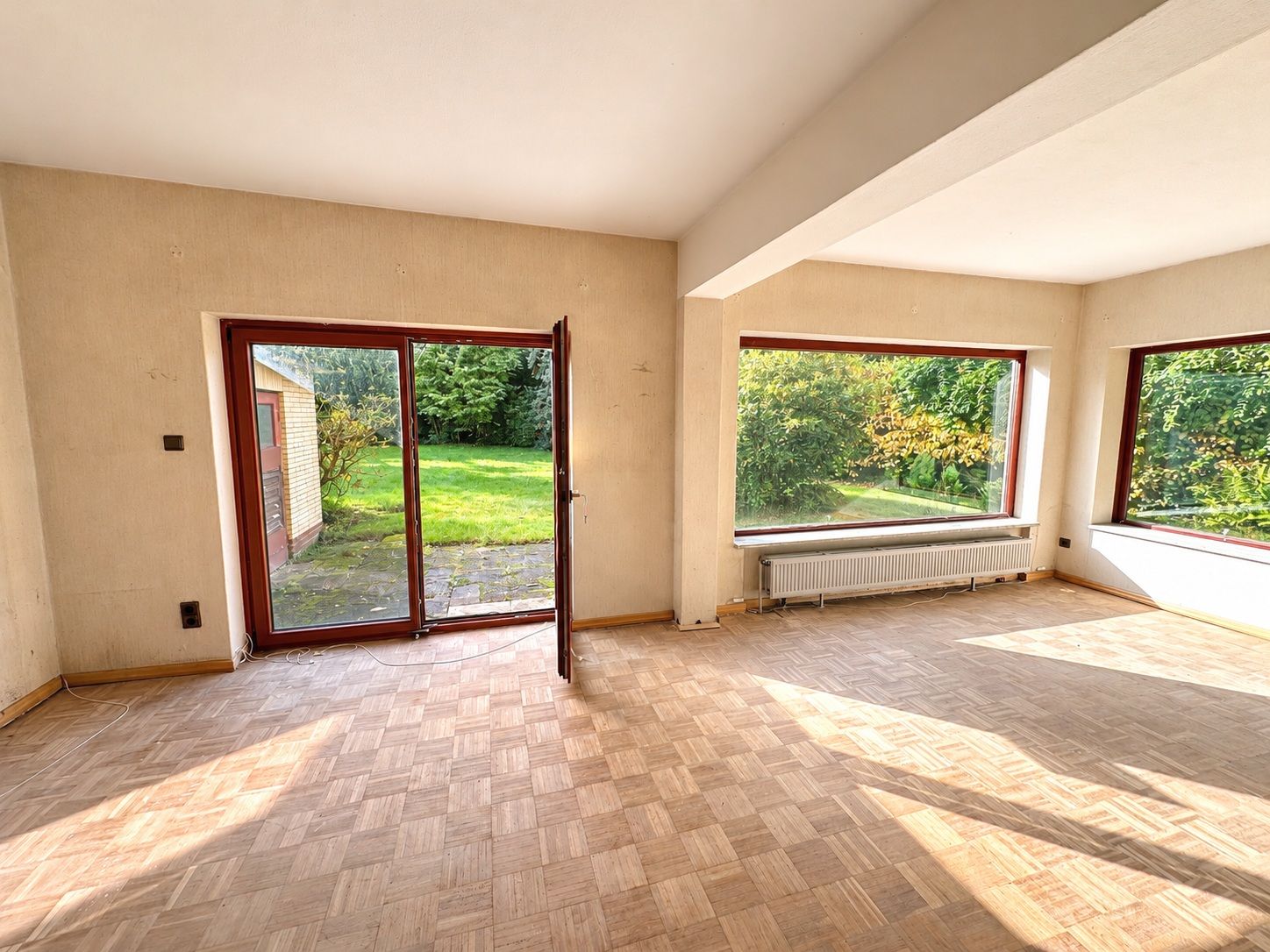 Helles Wohnzimmer mit Parkett, großen Fenstern und Terrassentür zum Garten.