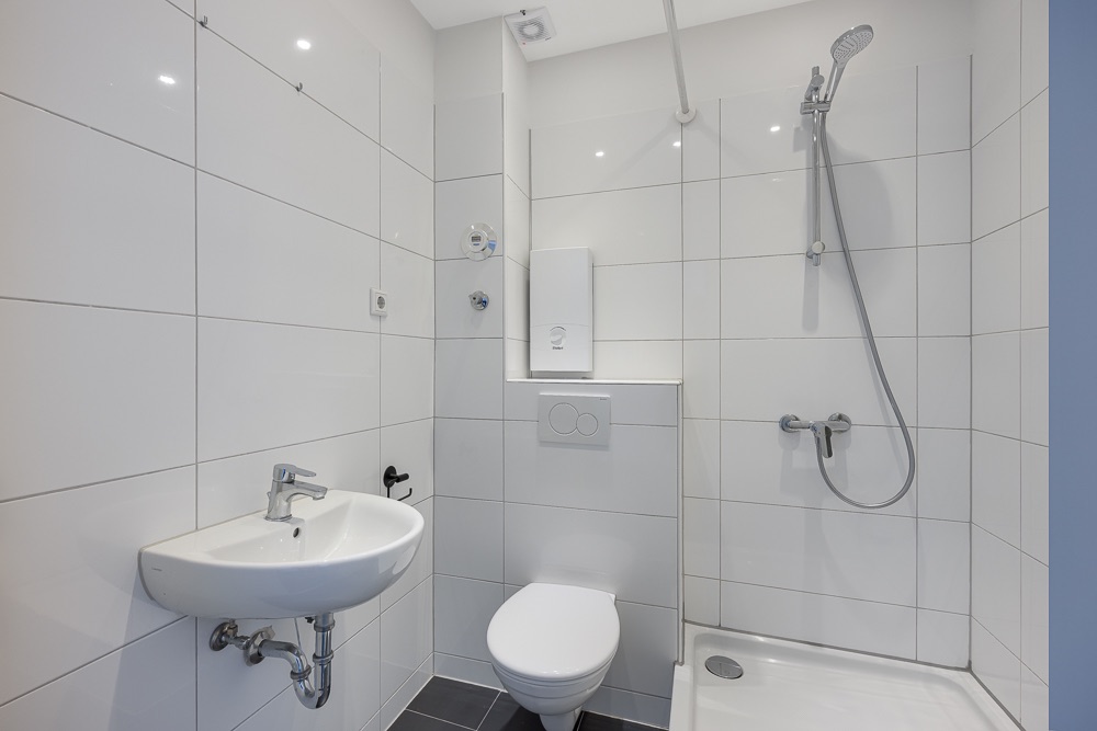 Modernes Badezimmer mit Dusche, WC und Waschbecken, alles in weiß gefliest.