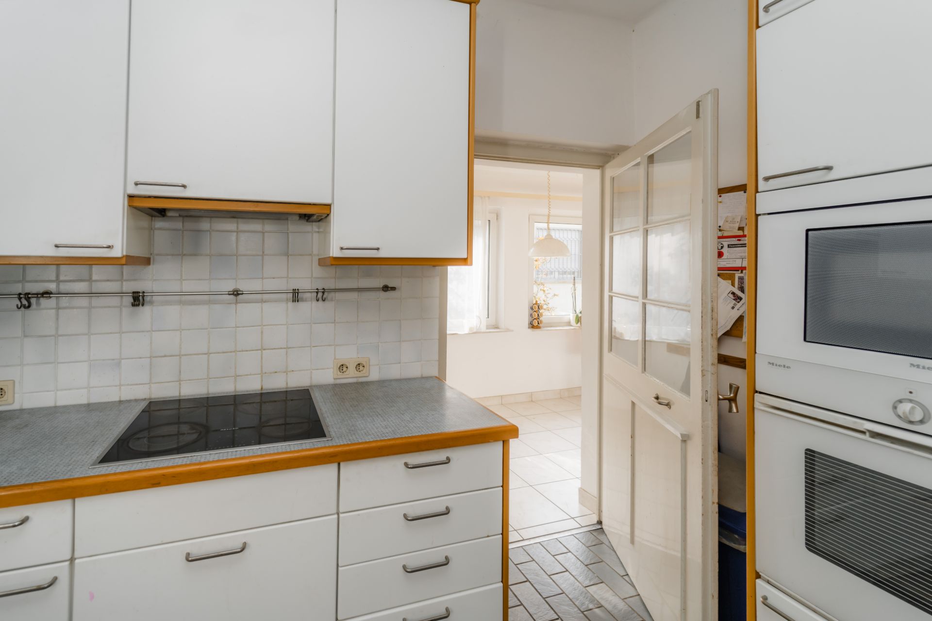 Moderne Küche mit weißen Schränken, Kochfeld und Blick in einen hellen Raum.