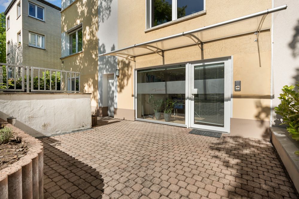 Gepflasterter Innenhof mit Glas-Schiebetür und Markise an einem Wohnhaus.