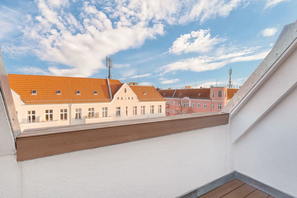 Kleine Dachterrasse mit Blick auf Häuser mit roten Dächern und blauem Himmel.