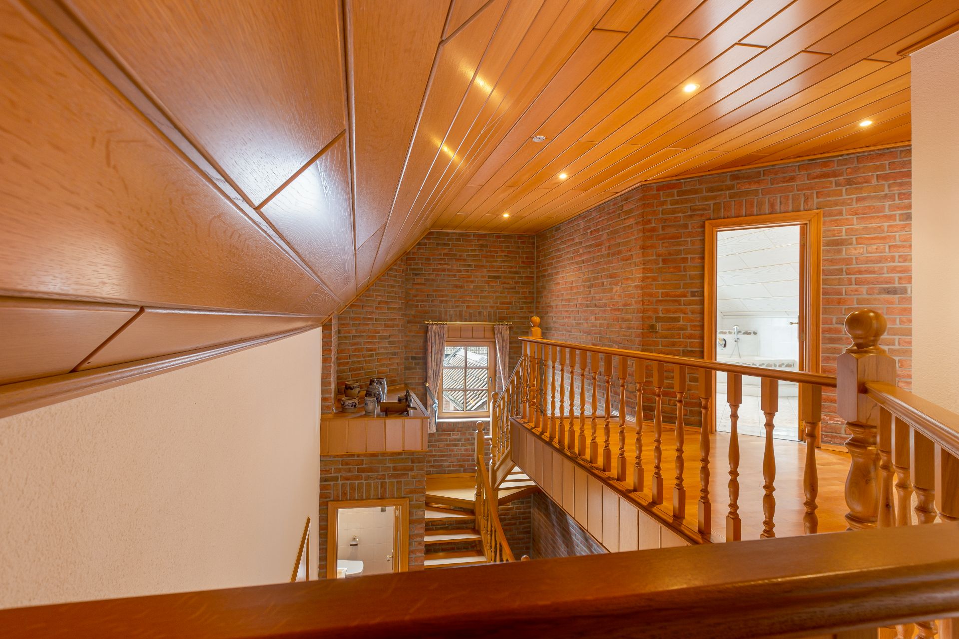 Holztreppe mit Geländer, Backsteinwände und Holzdecke in einem Wohnhaus, Fenster im Hintergrund.