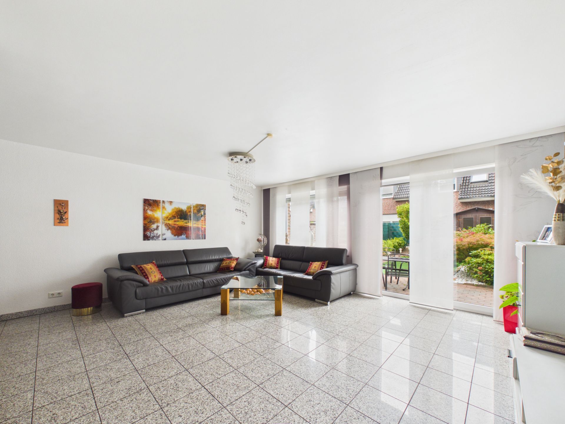 Helles Wohnzimmer mit zwei schwarzen Sofas, Glastisch und großen Fenstern zum Garten.