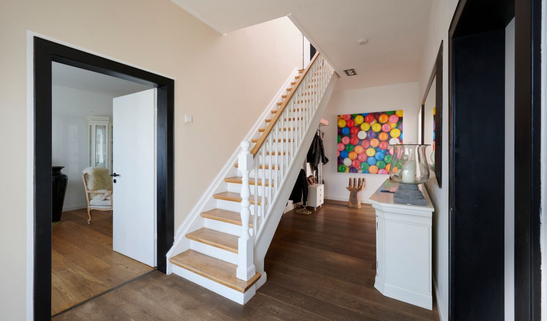 Hausflur mit Holztreppe, weißem Sideboard und buntem Bild an der Wand.