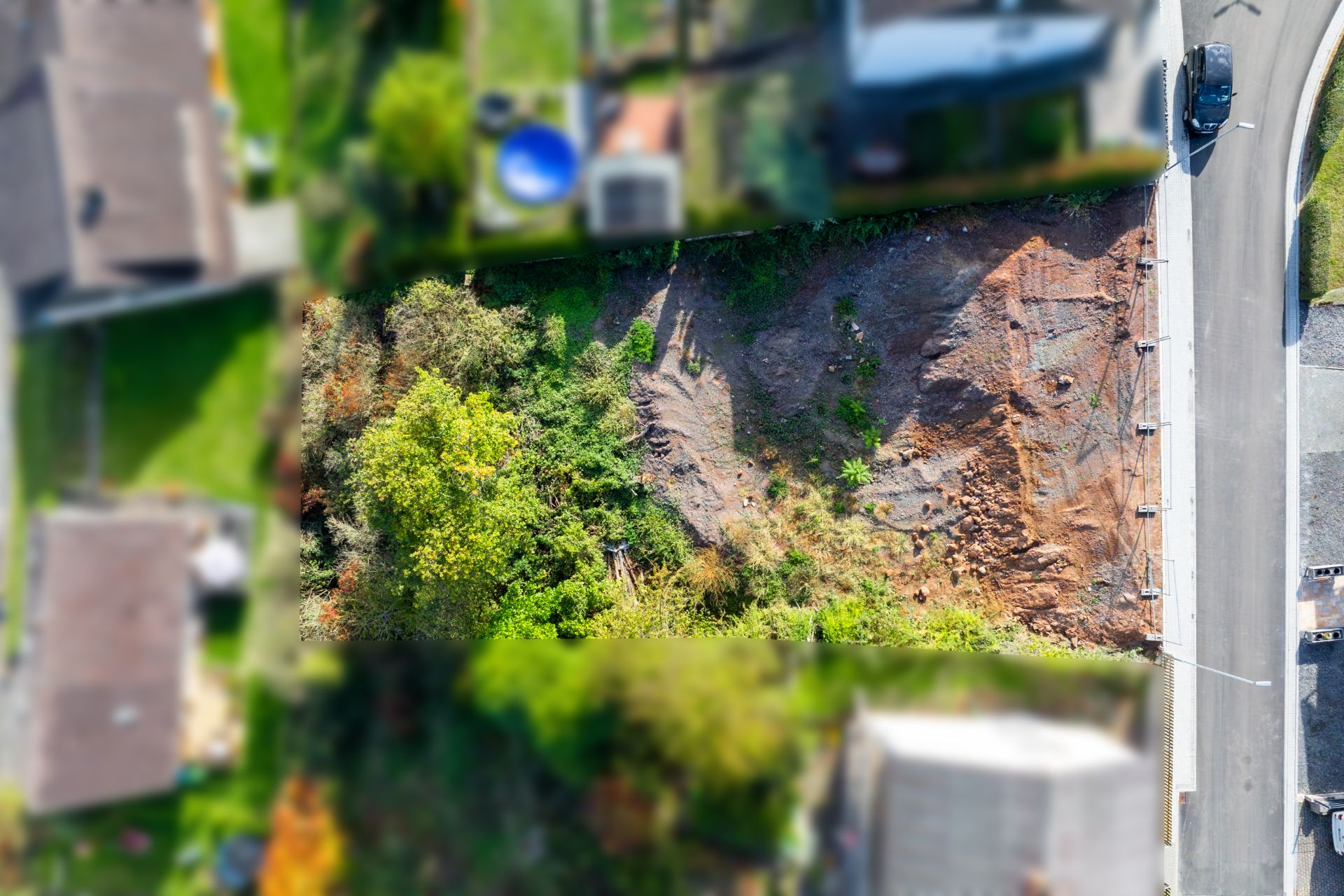 Luftaufnahme eines unbebauten Grundstücks mit Bäumen und Erde an einer Straße.