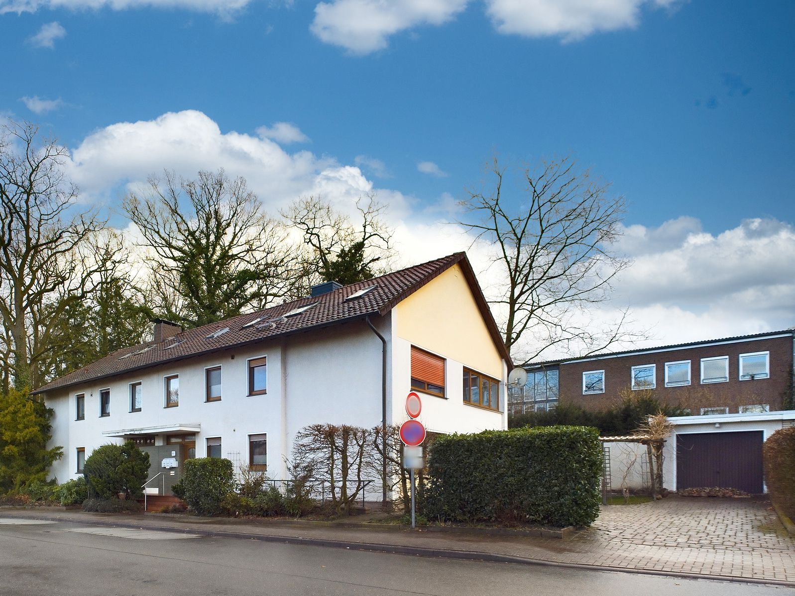 Weißes Wohnhaus mit Satteldach und Vorgarten an einer Straße, daneben eine Garage.