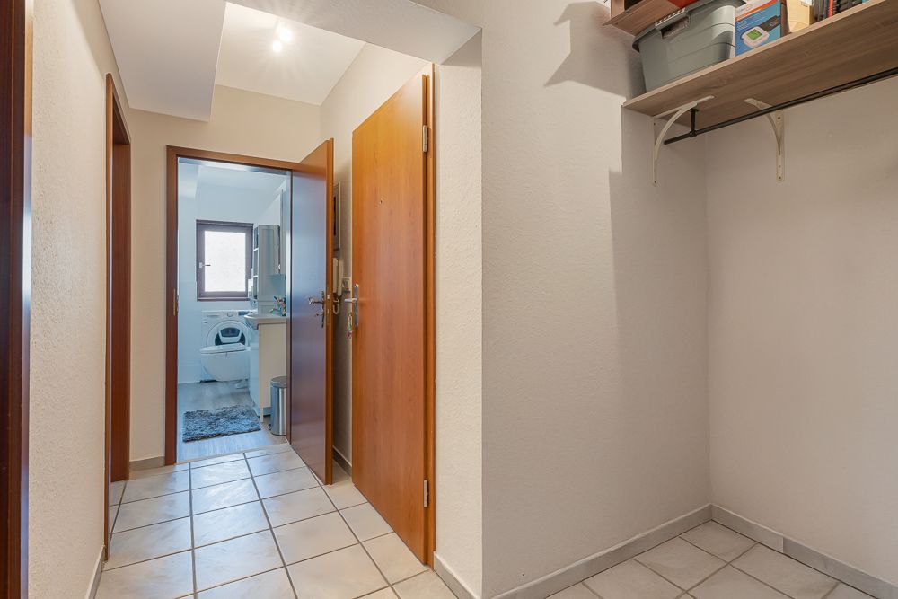 Heller Flur mit offener Tür zum Badezimmer, gefliester Boden, Wandregal mit Kisten.