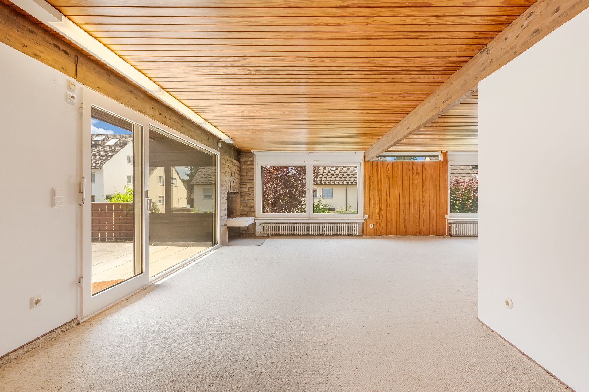 Helles Wohnzimmer mit Holzdecke, großen Fenstern und Zugang zur Terrasse.