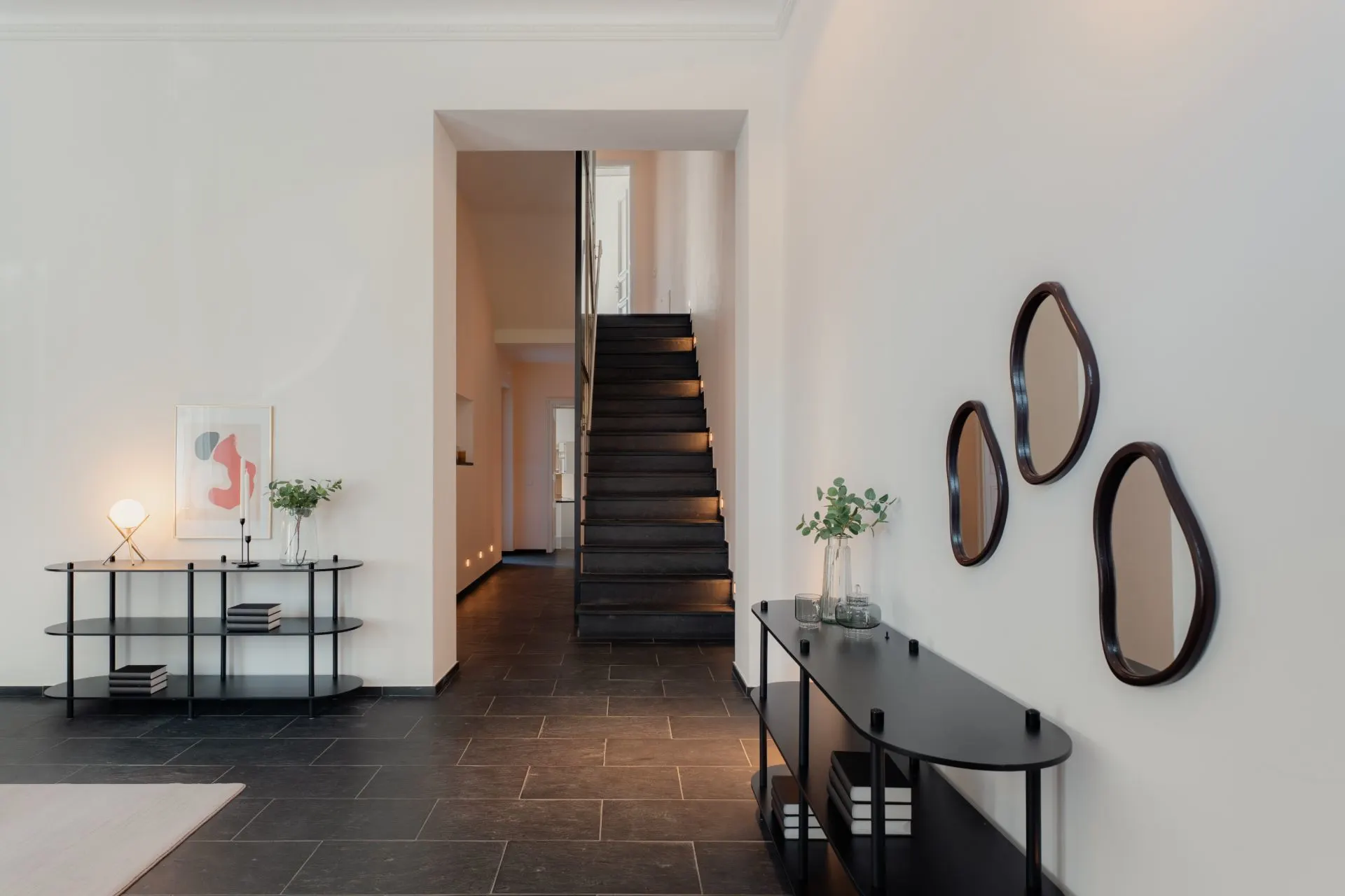 Moderner Flur mit schwarzer Treppe, Wandspiegeln und minimalistischen Sideboards.