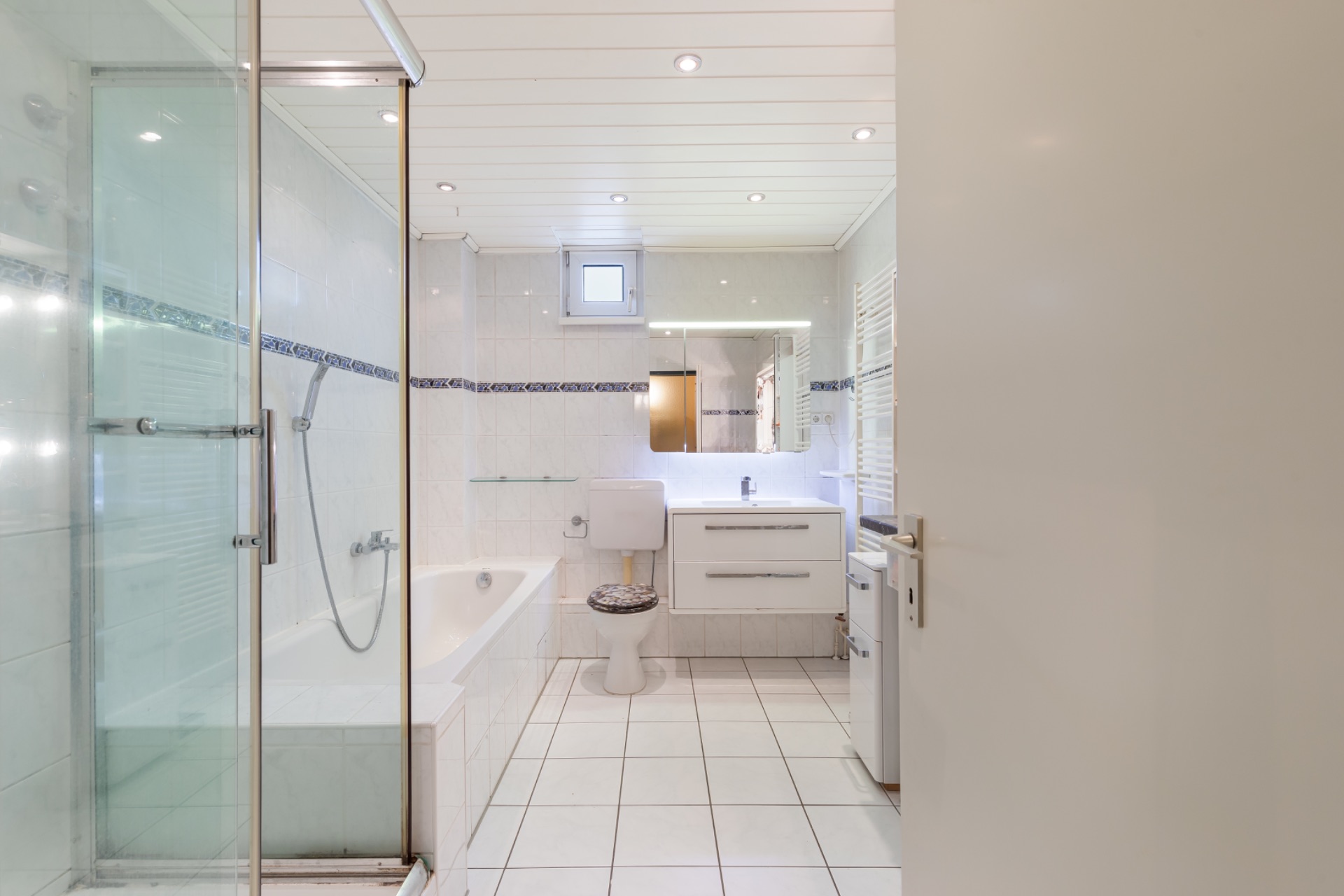 Helles Badezimmer mit Badewanne, Dusche, WC, Waschbecken und beleuchtetem Spiegel.