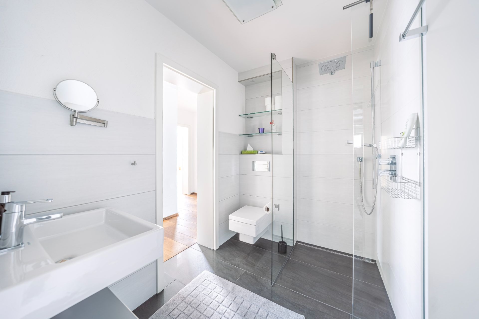 Modernes, helles Bad mit Waschbecken, WC und bodengleicher Dusche hinter Glaswand.
