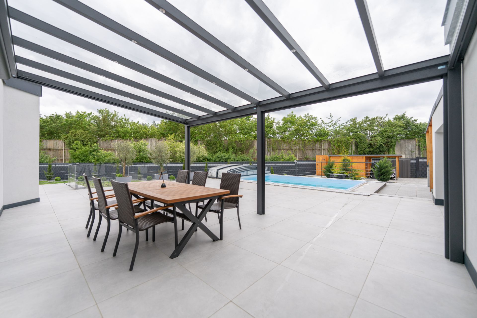 Überdachte Terrasse mit Esstisch und Stühlen, Blick auf einen Pool im Garten.
