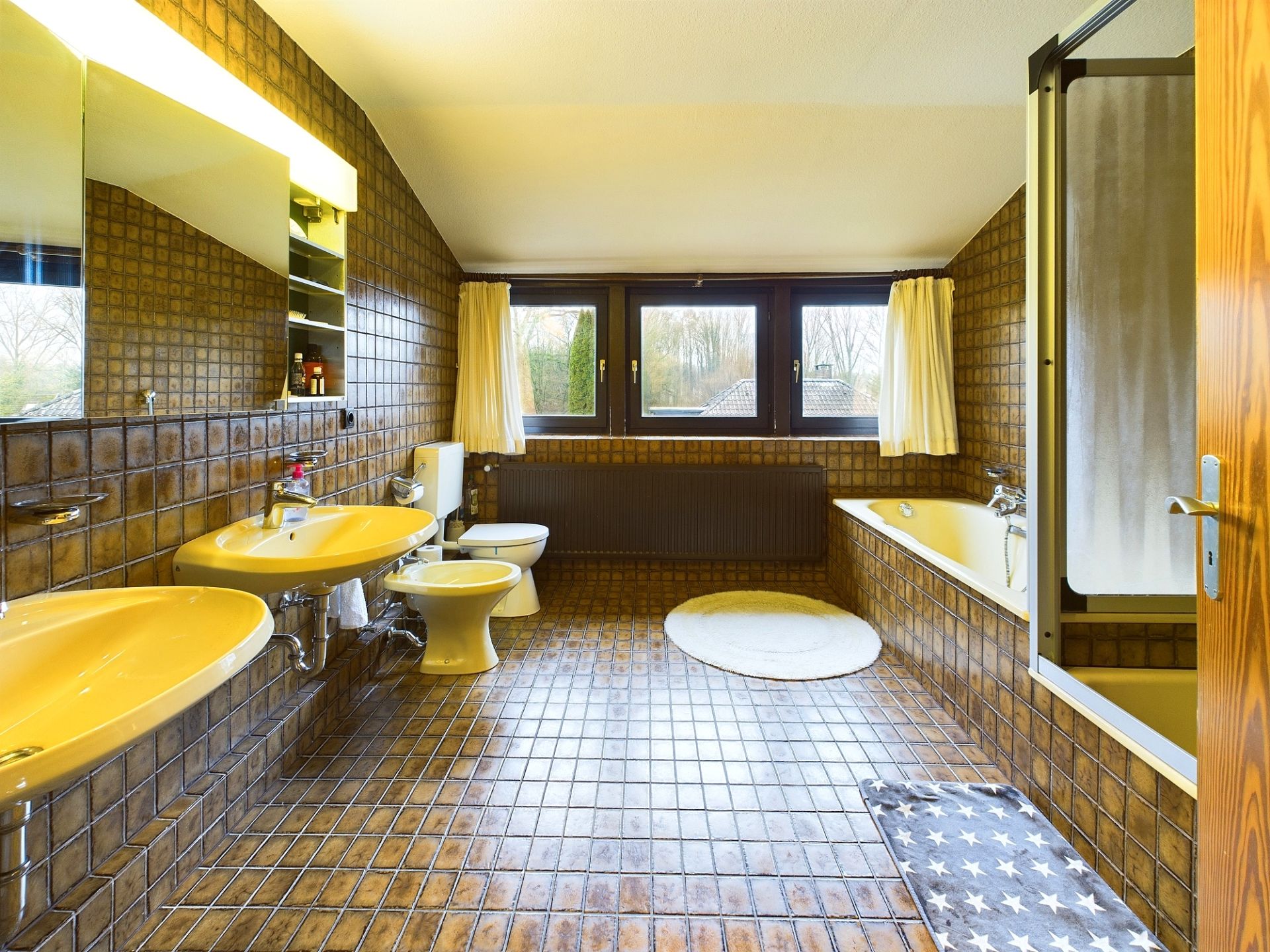 Großes Badezimmer mit zwei Waschbecken, Toilette, Badewanne, Dusche und drei Fenstern.
