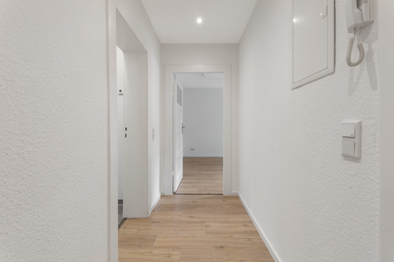 Heller Flur mit weiß gestrichenen Wänden und Holzfußboden in einer Wohnung.