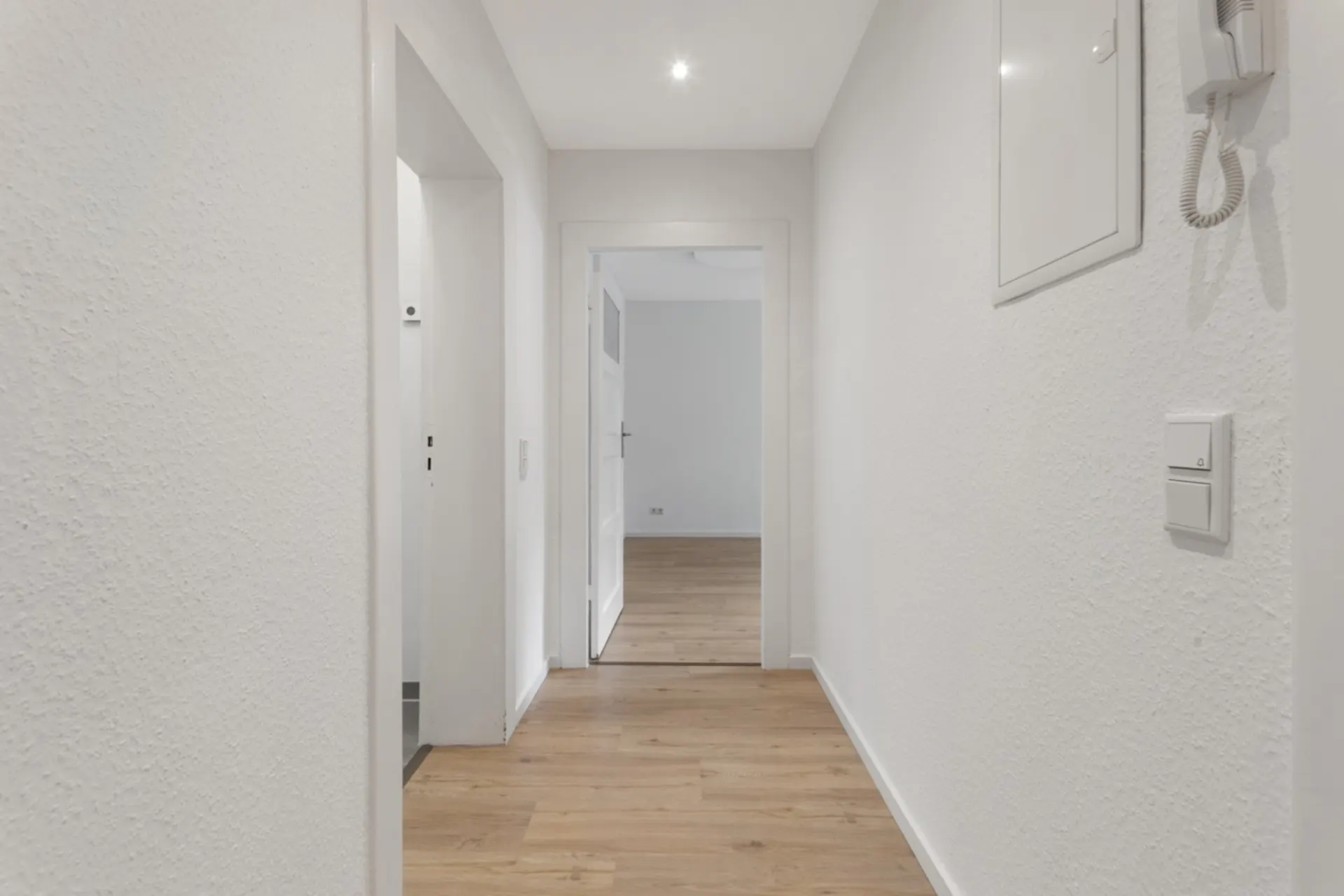 Heller Flur mit weiß gestrichenen Wänden und Holzfußboden in einer Wohnung.