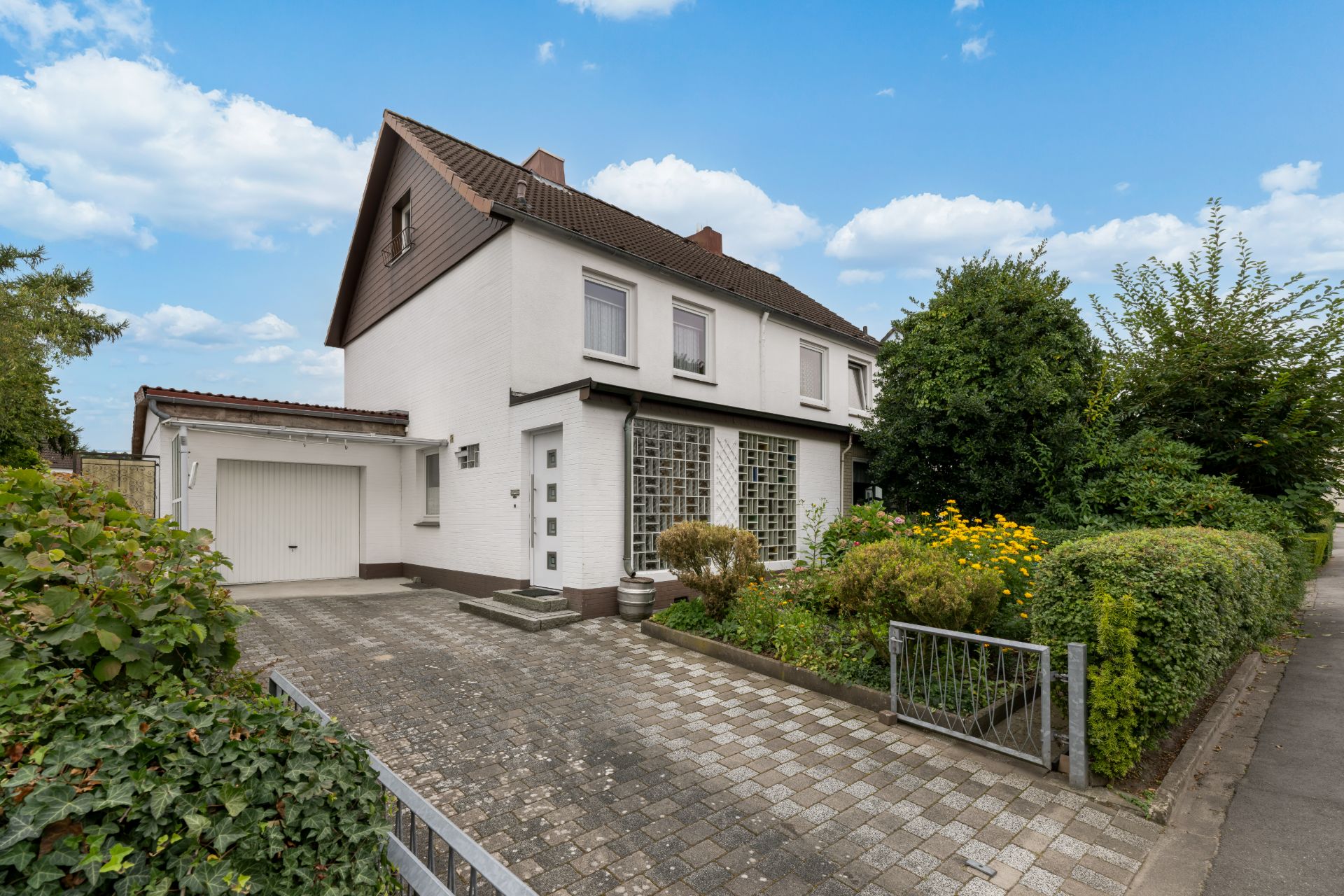 Zweistöckiges Einfamilienhaus mit Garage, gepflasterter Einfahrt und kleinem Vorgarten.