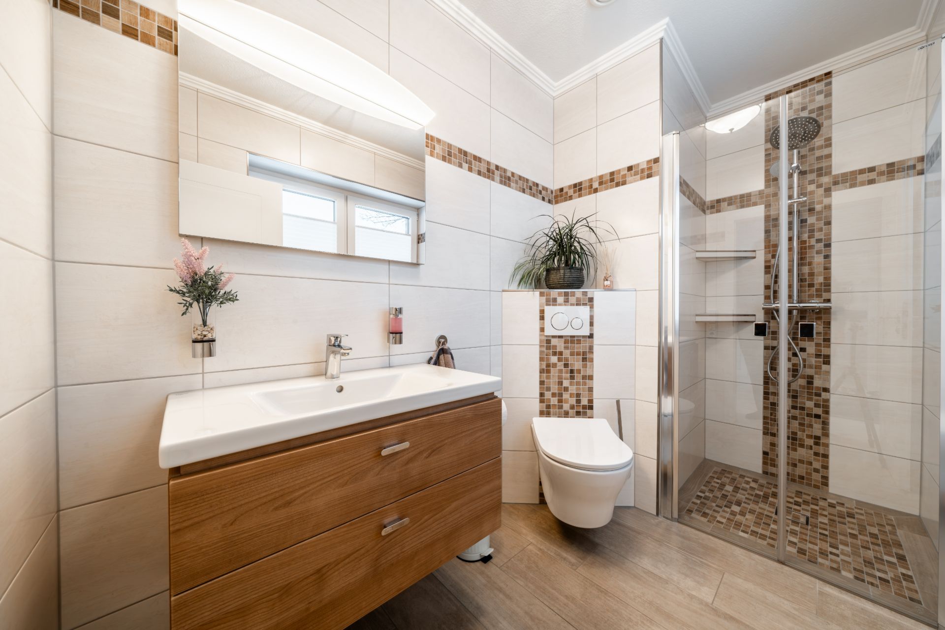 Modernes Badezimmer mit Waschbecken, Wandtoilette, Spiegelschrank und Dusche mit Glastüren.