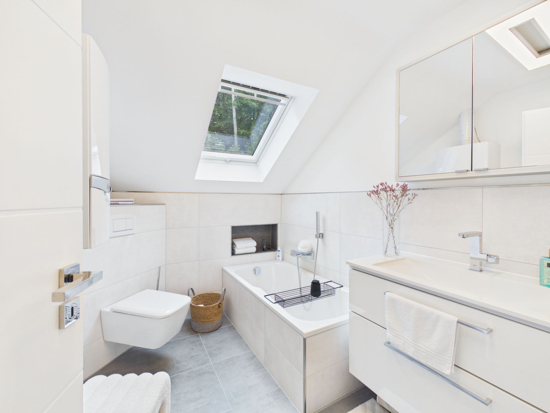 Modernes Badezimmer mit Badewanne, Wandtoilette, Waschbecken und Dachfenster.