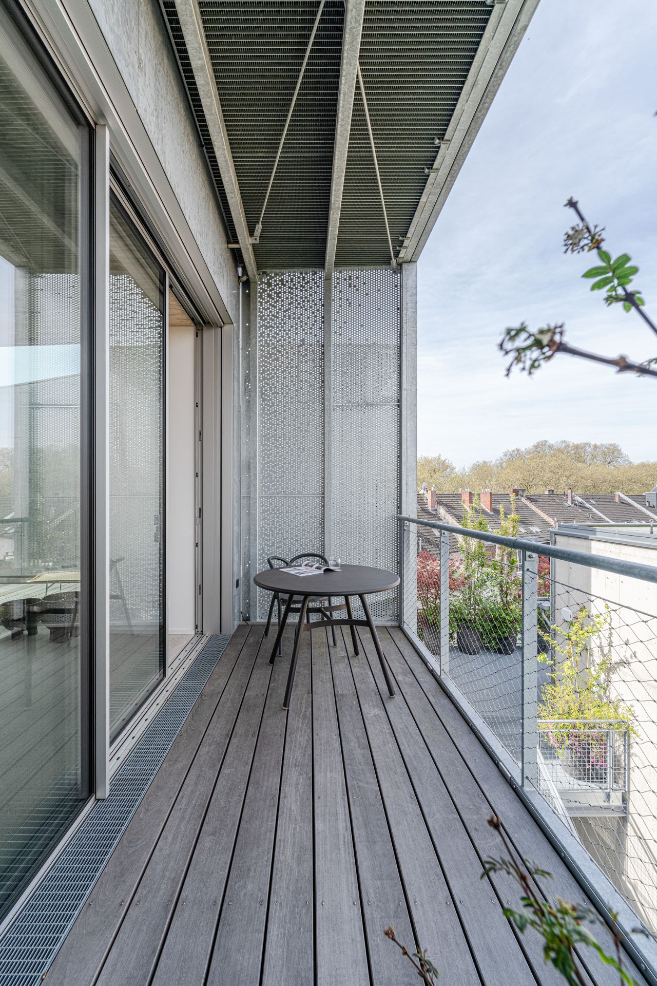 Moderner Balkon mit Holzboden, Tisch und zwei Stühlen, Blick auf Nachbarhäuser.