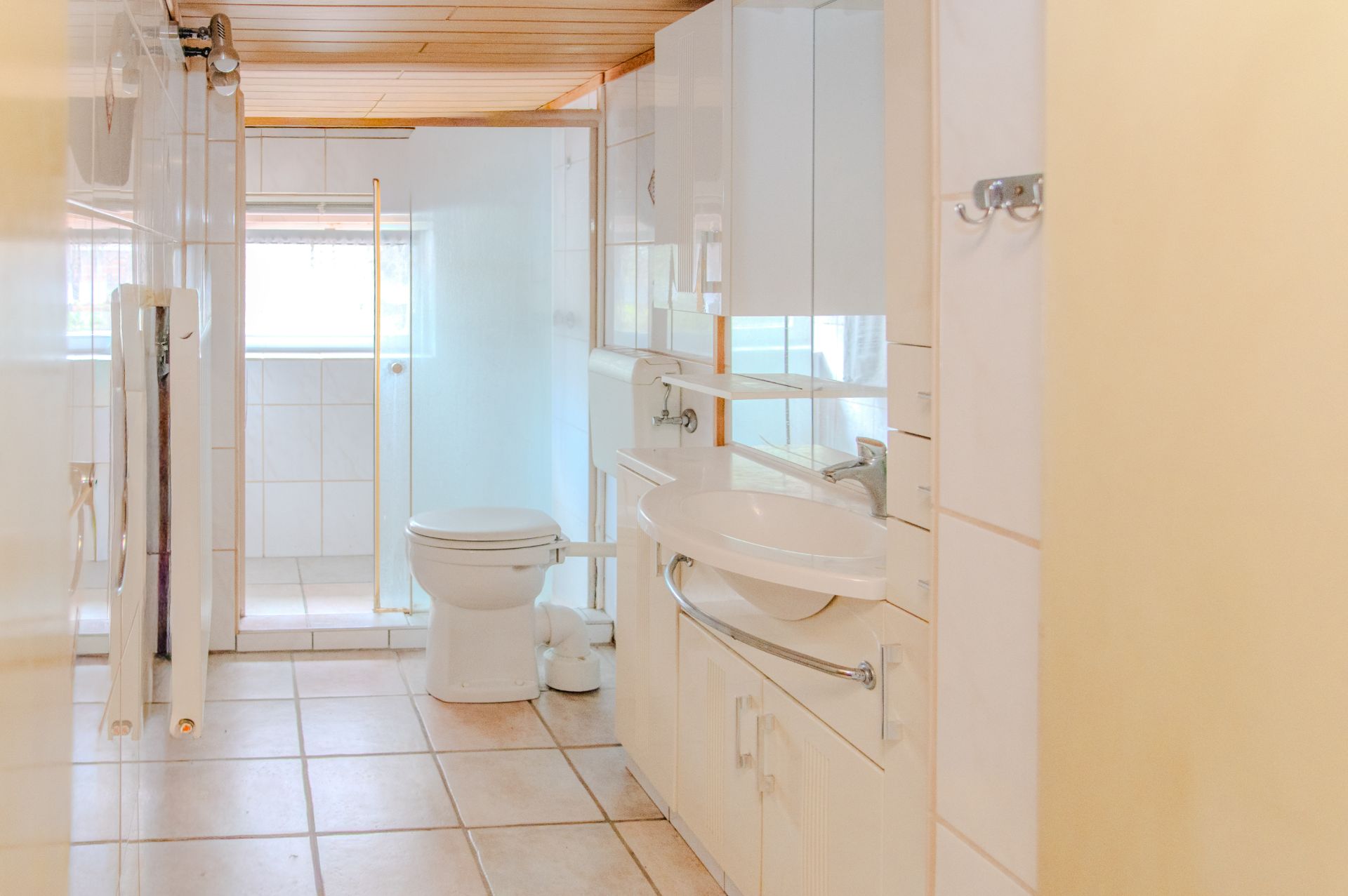 Modernes Badezimmer mit Toilette, Waschbecken, Dusche und hellen Fliesen.